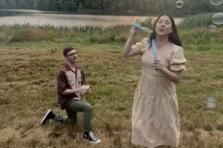 ジョナサン・ベネットがひざまずき、キャンディス・キングが野原でシャボン玉を吹いている。