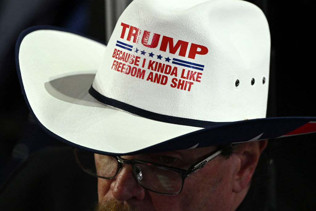 A person wearing a white cowboy hat with the text &quot;TRUMP BECAUSE I KINDA LIKE FREEDOM AND SHIT&quot; printed on it