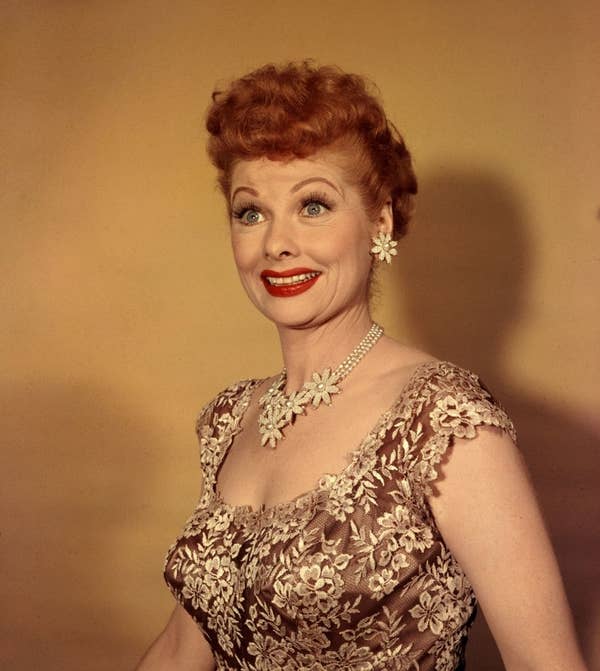 Lucille Ball smiles while wearing a floral lace dress, matching floral necklace, and earrings