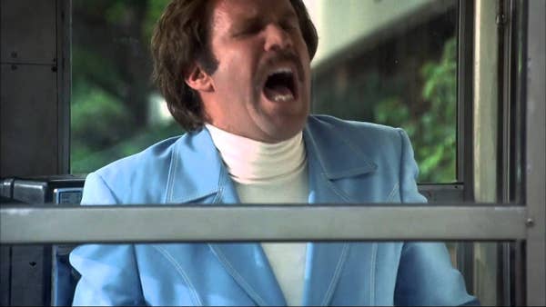 Will Ferrell as Ron Burgundy in a blue suit and white turtleneck, yelling on a bus, from the movie "Anchorman"