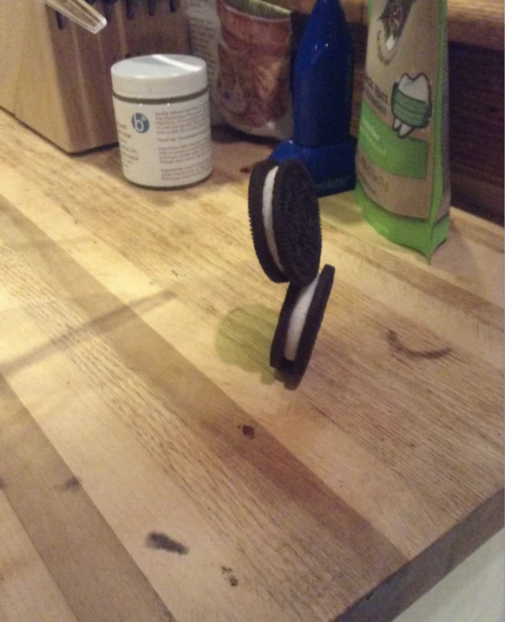 Two Oreo cookies balancing on a kitchen counter, with various kitchen items in the background