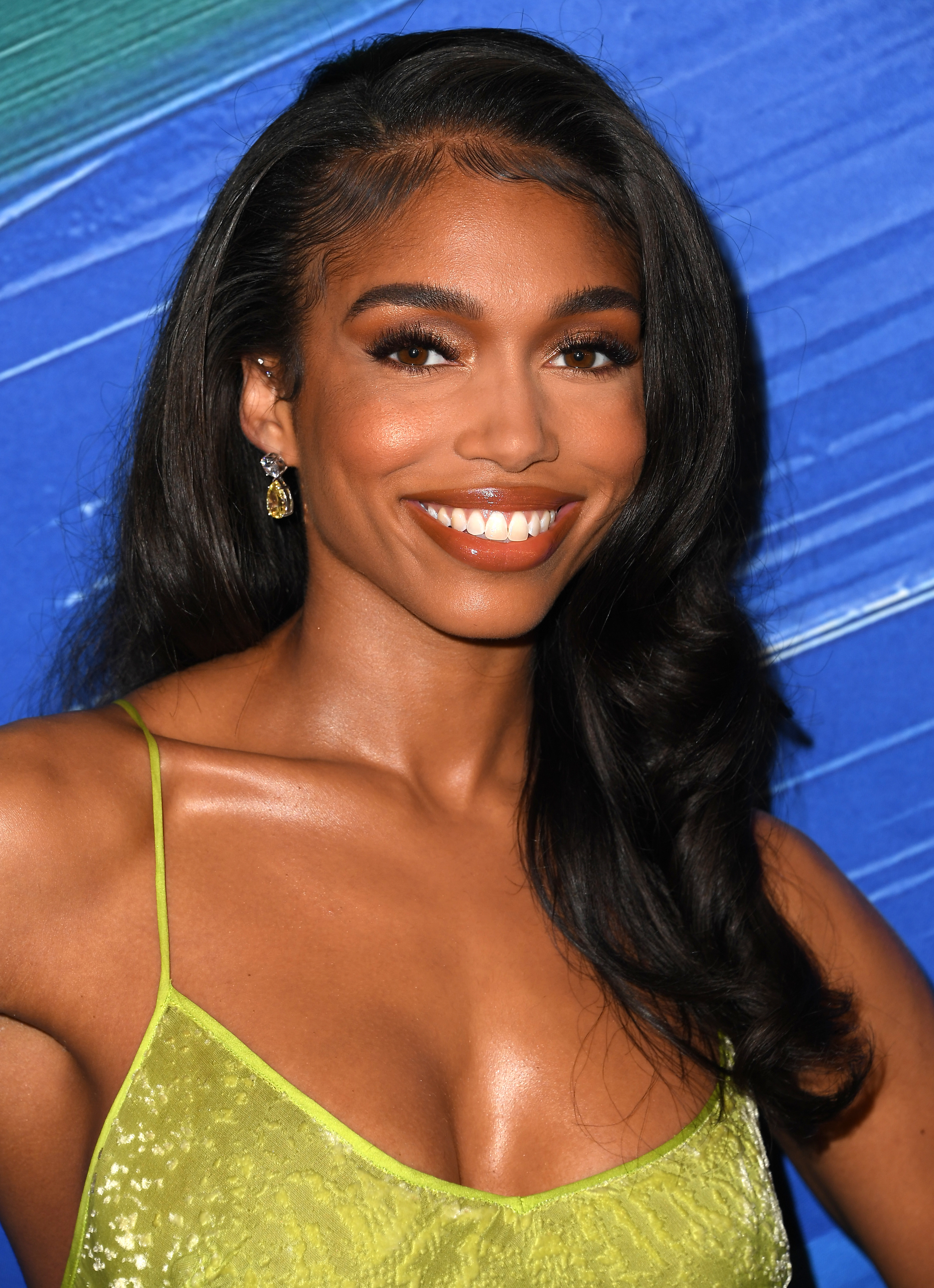 Lori Harvey smiles at the camera wearing a textured green dress with thin straps