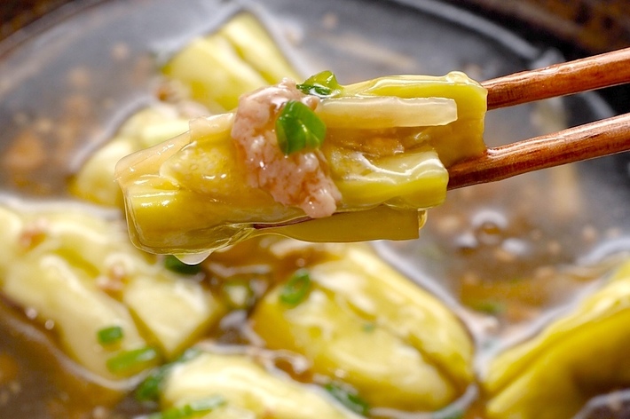 箸で持ち上げられた煮卵入りの料理。スープの中にいくつかの具が見える。