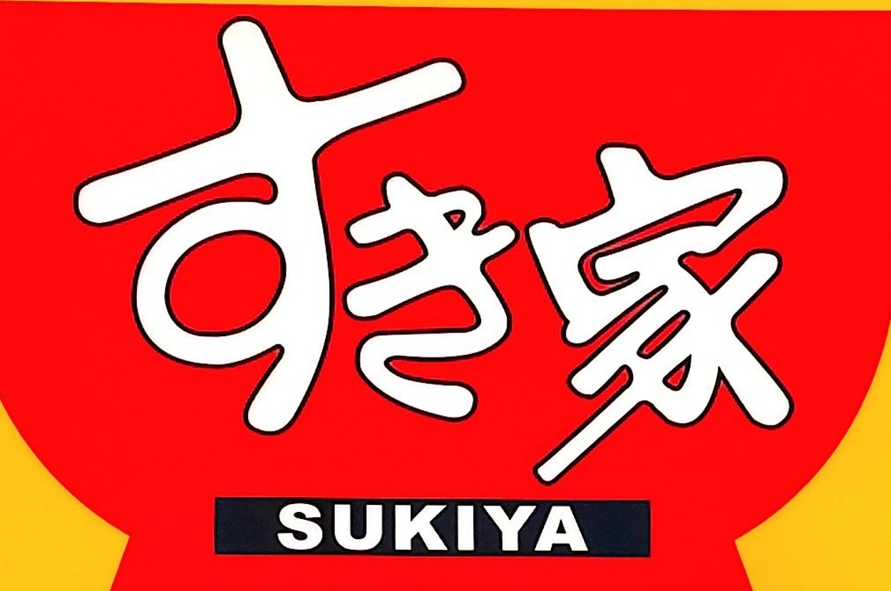 A sign with the text "SUKIYA" below large Japanese characters. The sign is above a building entrance
