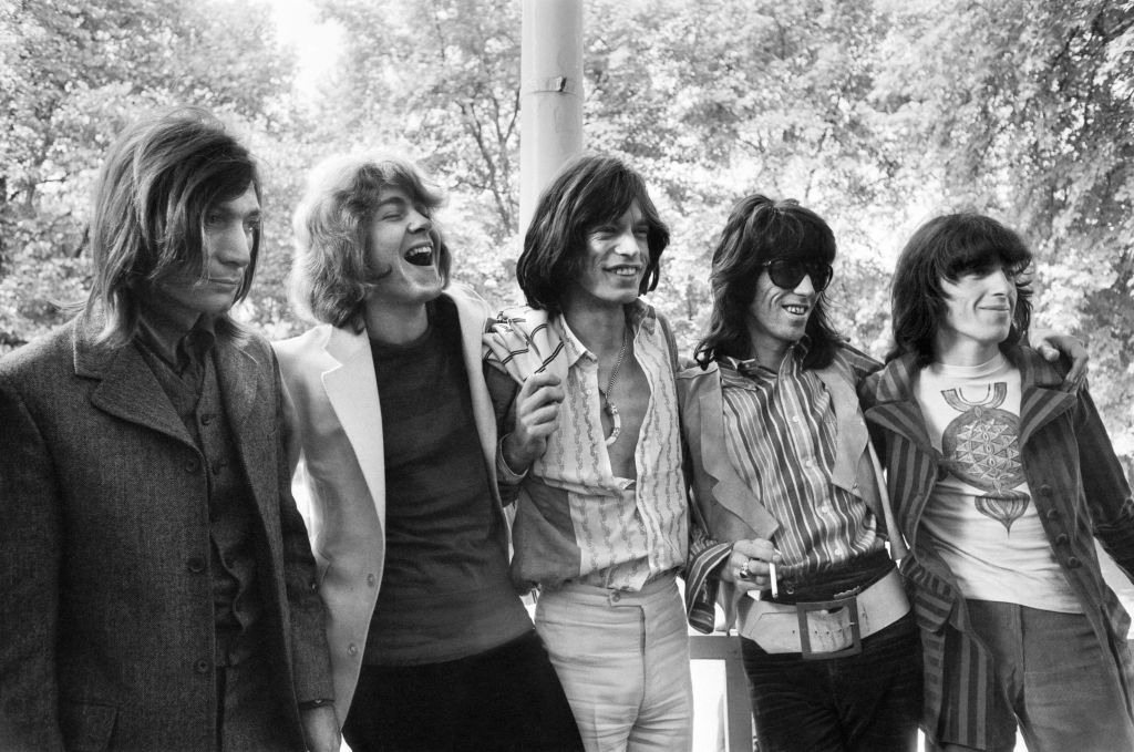 A group photo featuring five members of The Rolling Stones: Charlie Watts, Mick Taylor, Mick Jagger, Keith Richards, and Bill Wyman, in casual clothing outdoors