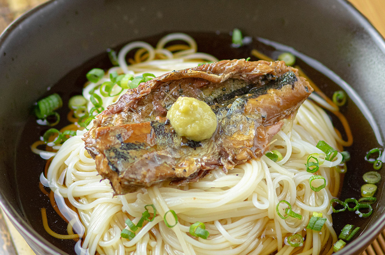 器に盛られたそばの上にさんまのかば焼きとわさびがのっている料理。細ねぎが周りに散らされている。