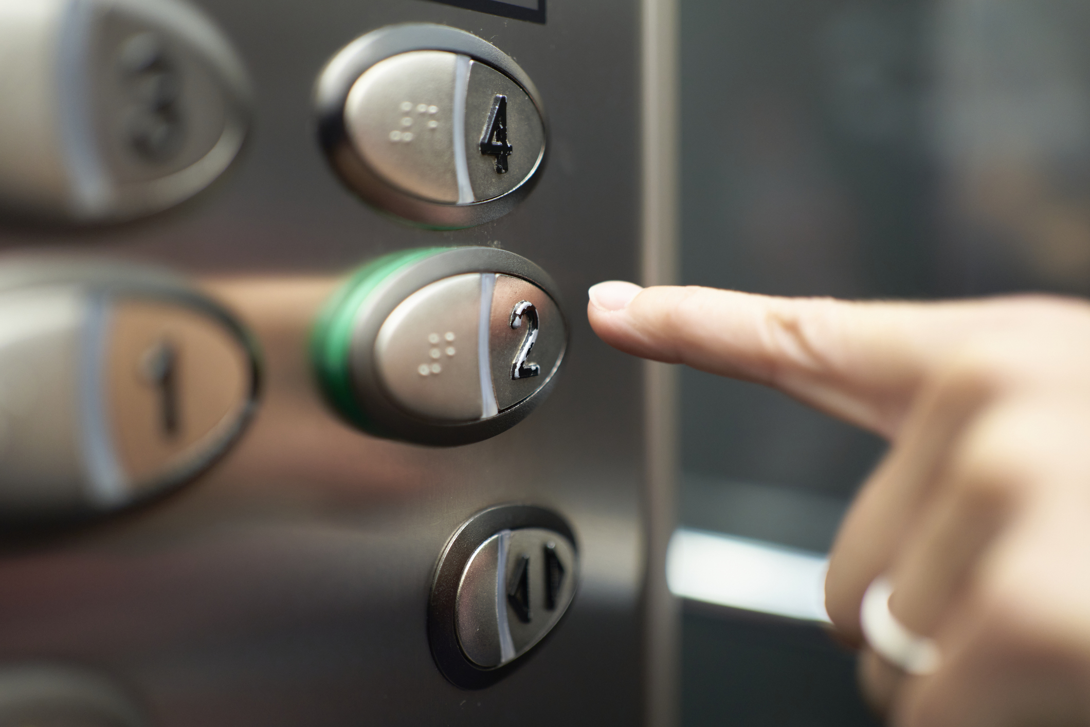 A finger presses the button for the second floor on an elevator control panel. The panel includes buttons for floors 4, 3, 2, and door controls