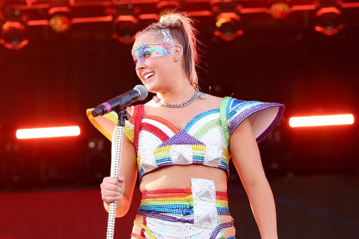 JoJo Siwa performs on stage in a colorful, futuristic outfit with rainbow accents and bold makeup