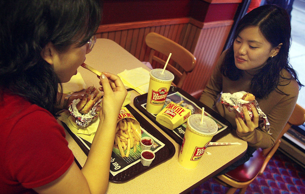 Two people are eating at a Wendy's fast food restaurant, with trays of fries, drinks, and burgers in front of them