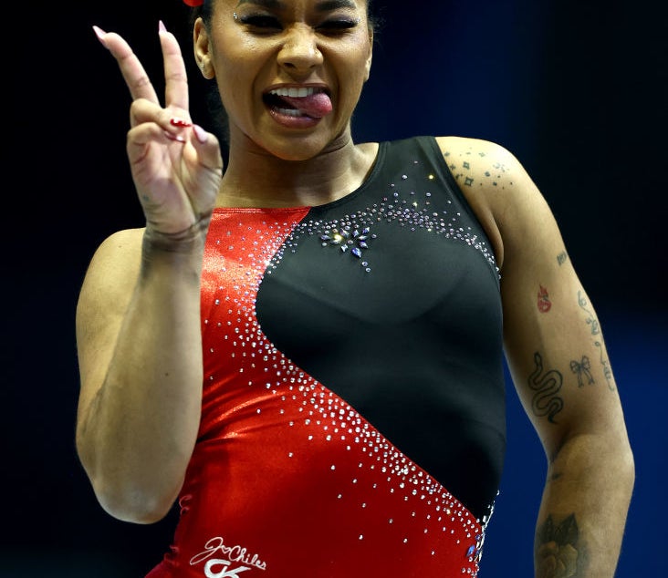 Jordan Chiles wearing a red and black gymnastics leotard, making a peace sign with her right hand and sticking out her tongue