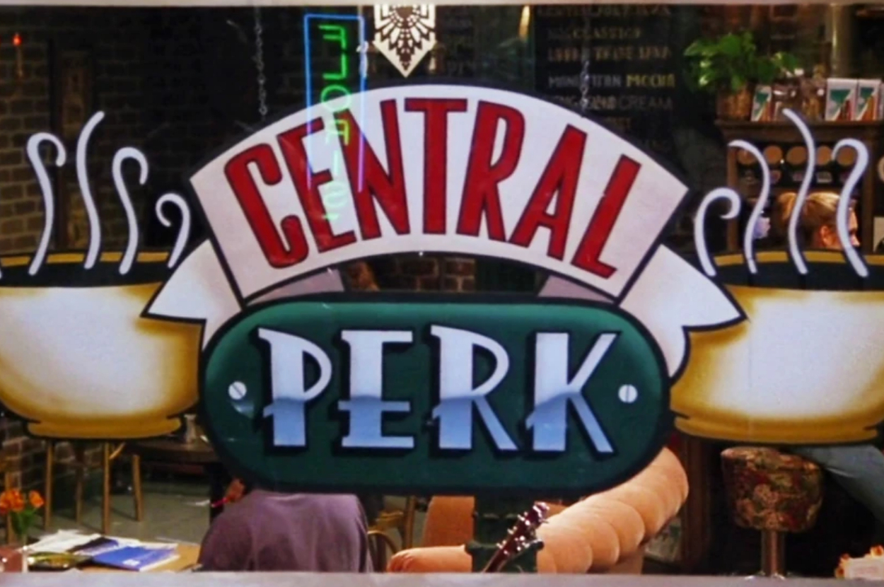 Central Perk sign from Friends TV show displaying "Central Perk" in bold letters, with a coffeehouse setting visible through the window