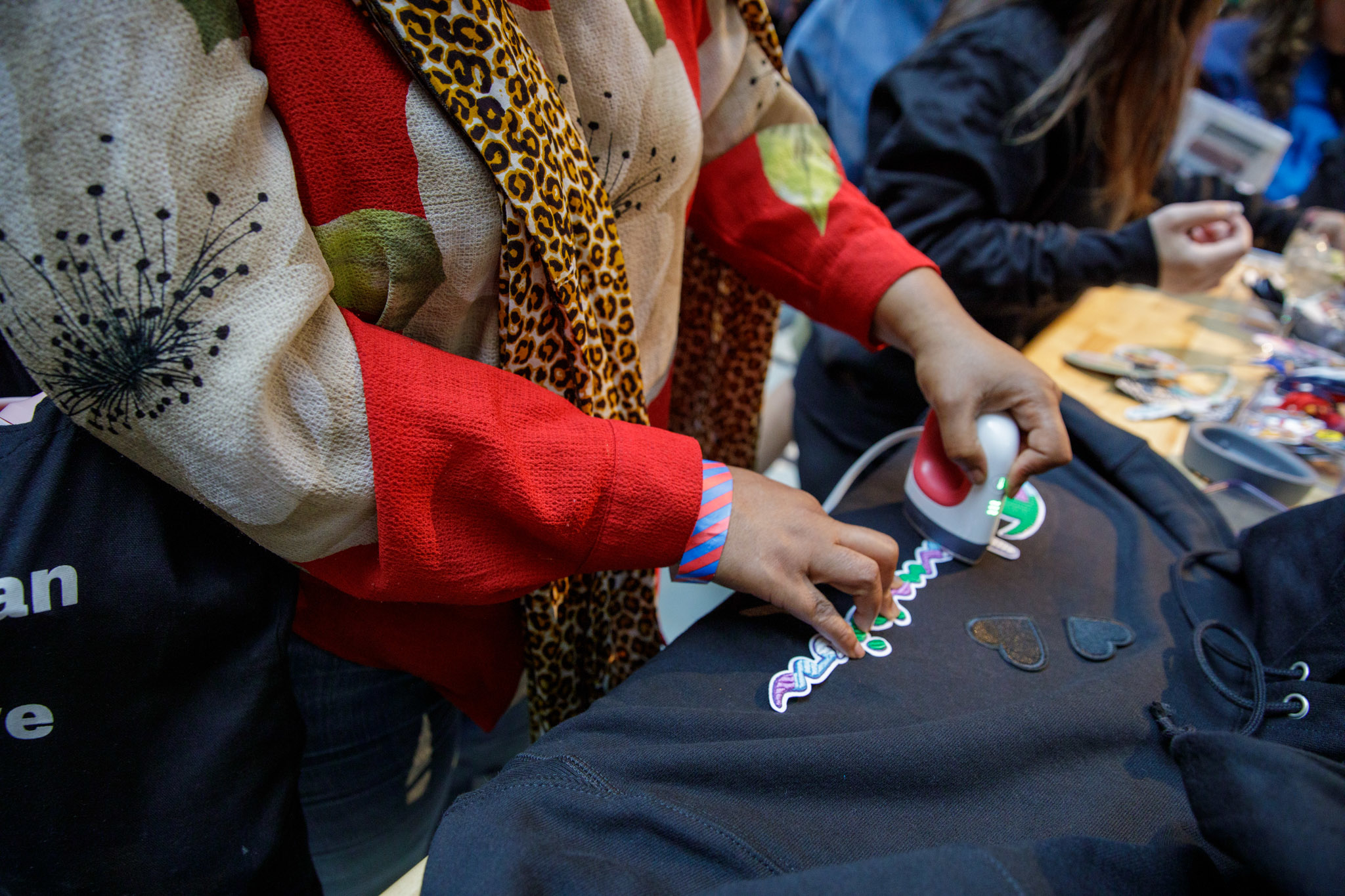 Person using a small iron to apply colorful patches to a black garment at a craft table