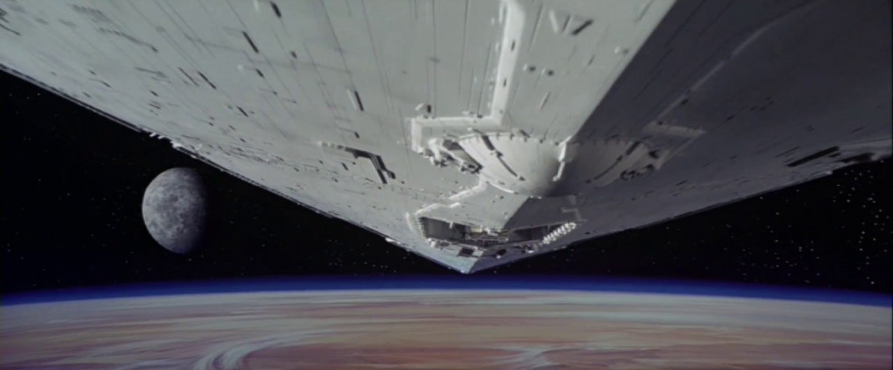 A massive spaceship flies over a planet with a moon in the distance, as depicted in a scene from Star Wars