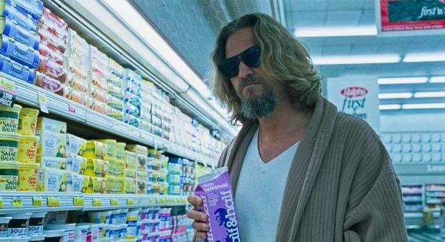 Jeff Bridges, wearing sunglasses, a white shirt, and a robe, holds a carton of half-and-half while standing in a grocery store aisle