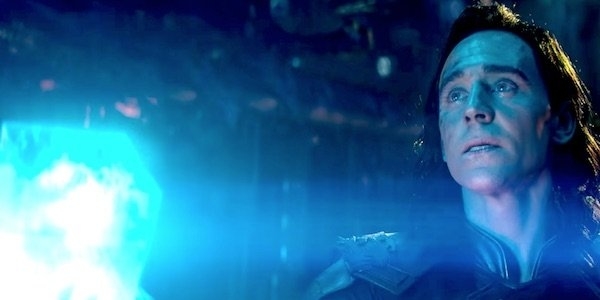Loki, wearing an armored outfit, gazes intently while surrounded by glowing blue light in a dark, mysterious setting