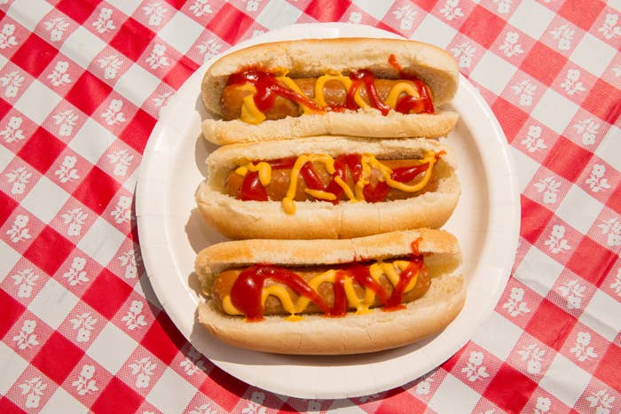 Three hot dogs with ketchup and mustard on a white plate placed on a checkered tablecloth