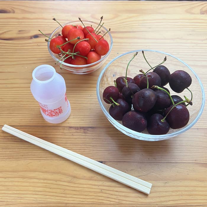 テーブルには、2つのボウルに入ったサクランボとヨーグルト飲料ボトル、箸があります。