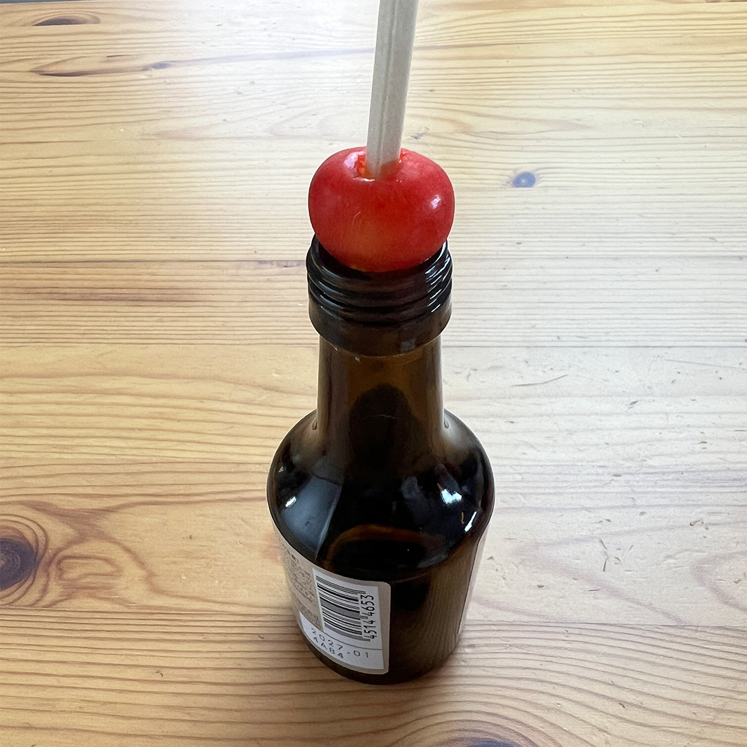 テーブル上の瓶の首に刺さったチェリーと割り箸が見えます。