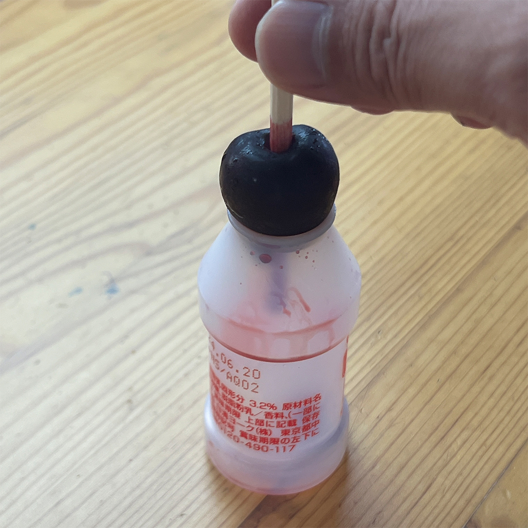 1つの手が、この飲み物のような小さなボトルの上部を持ち、木の棒を挿入している。