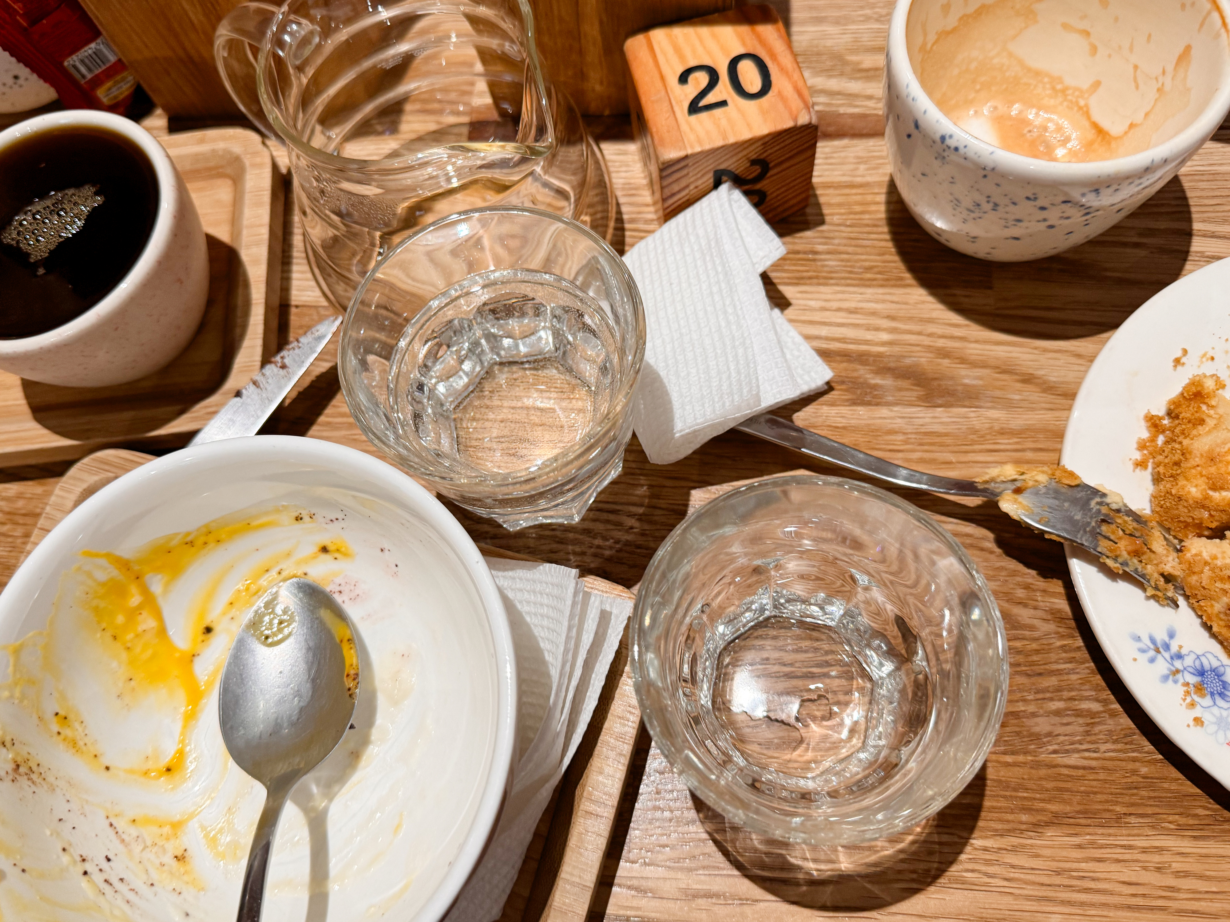 Table with empty plates, cups, and glasses seen close-up, alongside a napkin dispensary and a wooden block displaying the number &quot;20&quot;