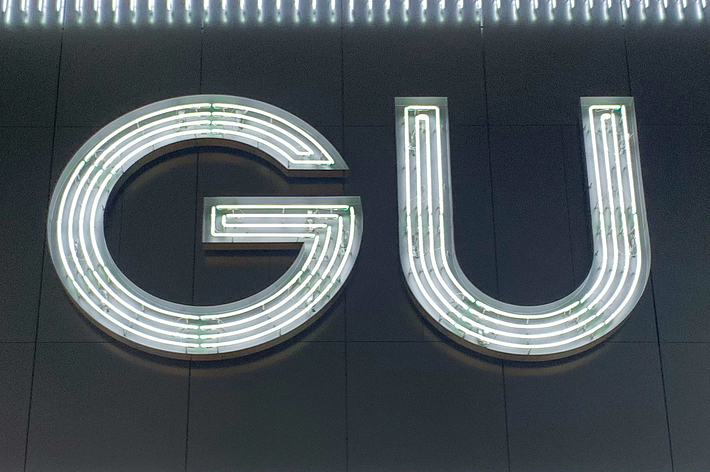 The image shows a neon-lit sign of the letters &ldquo;GU&rdquo; in a stylish, modern font, likely representing a store or brand