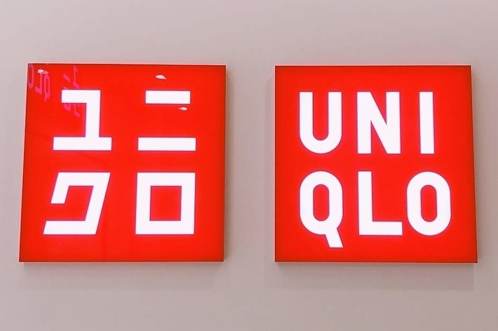 Two red squares with white text, one in Japanese characters and the other saying &ldquo;Uniqlo,&rdquo; mounted on a plain wall