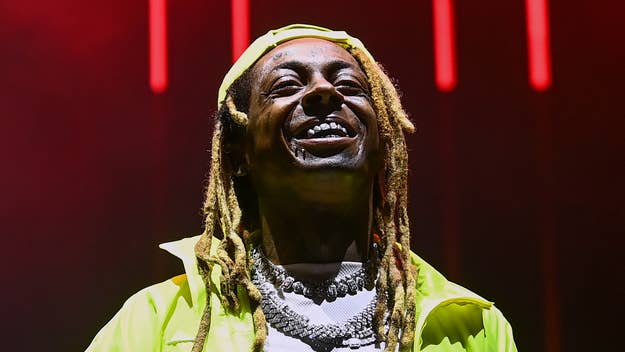 Lil Wayne smiles broadly on stage, wearing layered necklaces and a neon green jacket