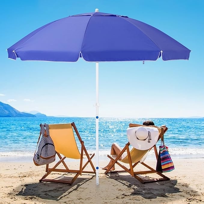 Two beach chairs under a blue umbrella by the ocean