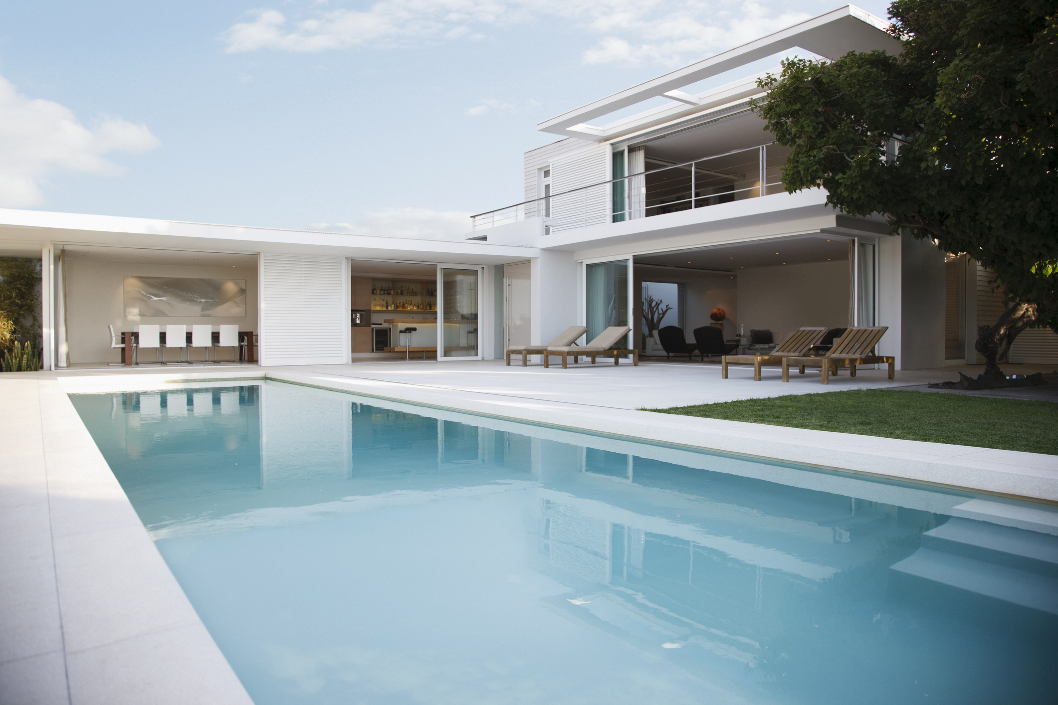 Modern, luxurious house with an expansive pool, outdoor seating area, and large windows connecting the indoor living spaces to the outdoors