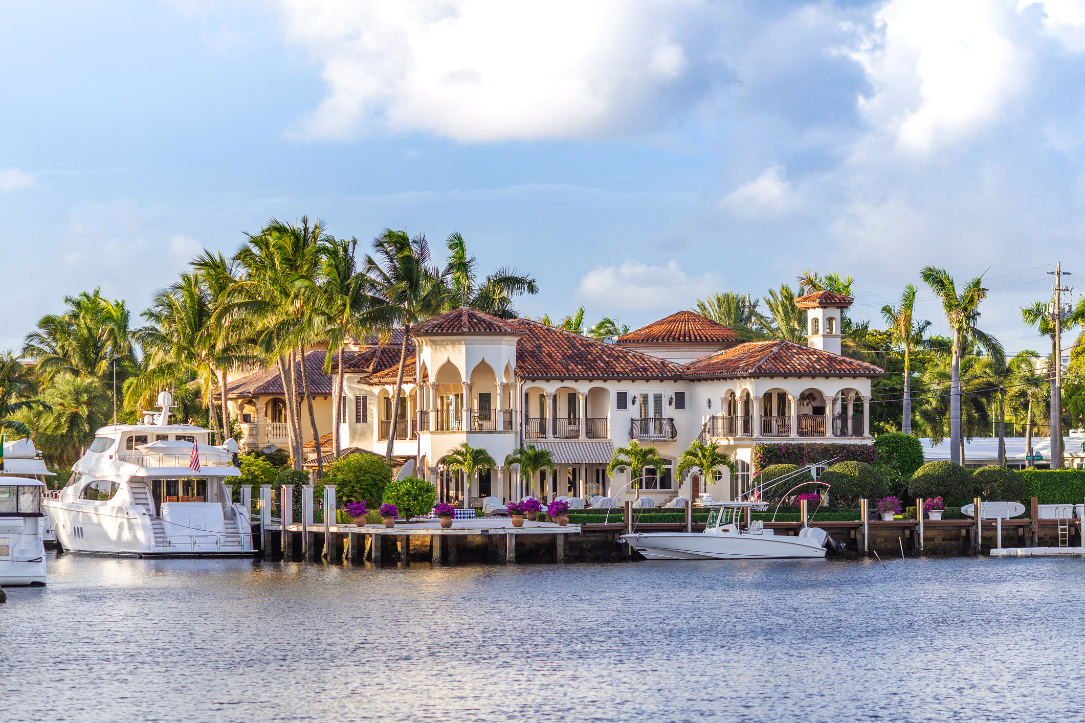 Luxurious waterfront mansion with archways, palm trees, and docked boats, showcasing opulent living. (Work & Money article context)