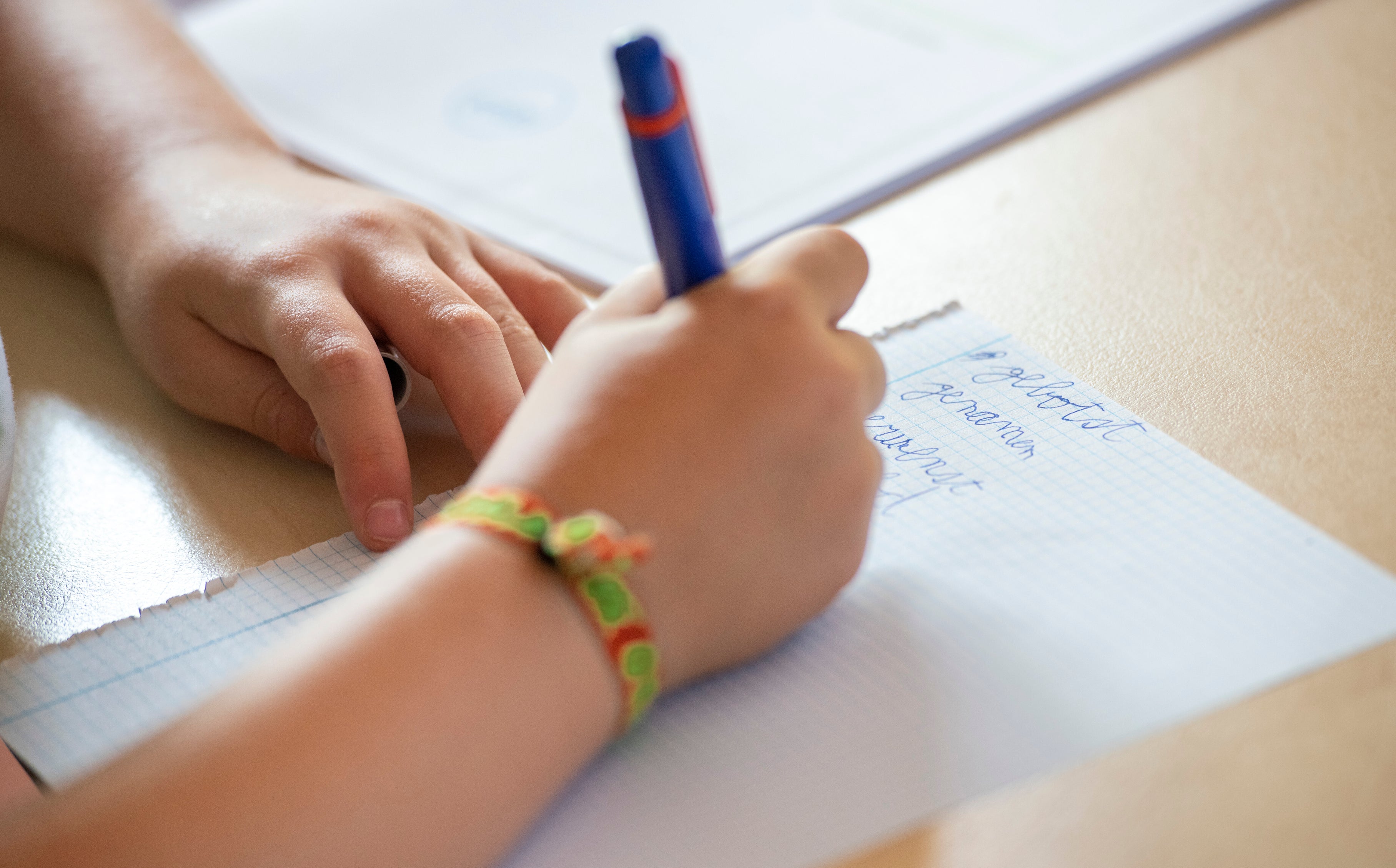 A child's hands are seen writing on a sheet of paper with a pen