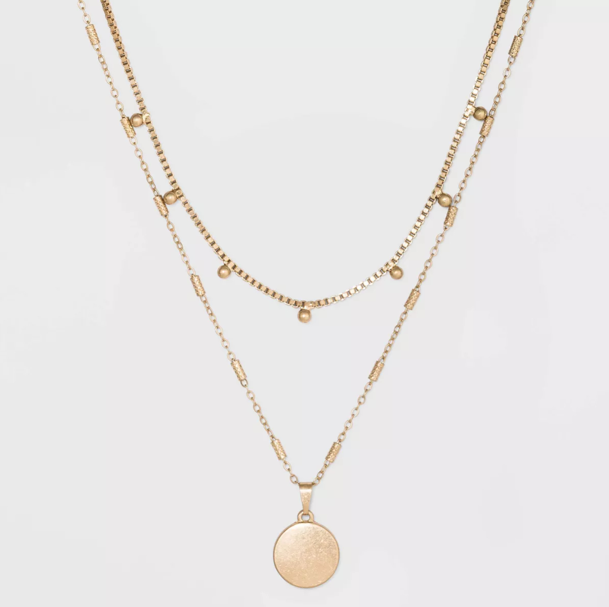 A layered gold necklace with three chains, one with small round beads and the bottom chain featuring a round gold pendant