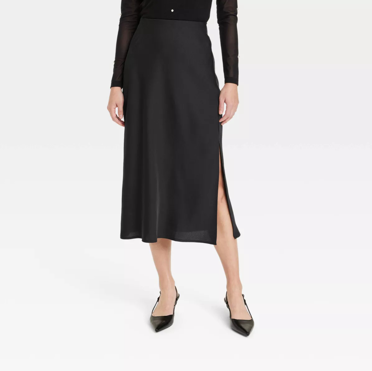 Person wearing a long, elegant black skirt with a slit up the side, black pointed-toe heels, and a black long-sleeve top
