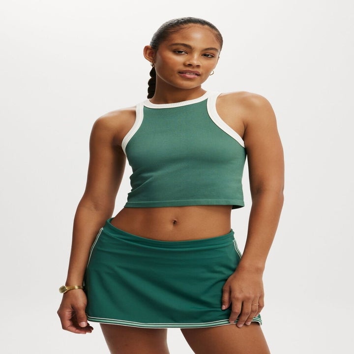 Woman in a sleeveless, fitted green top with white trim and a matching green mini skirt with white accents, posing confidently