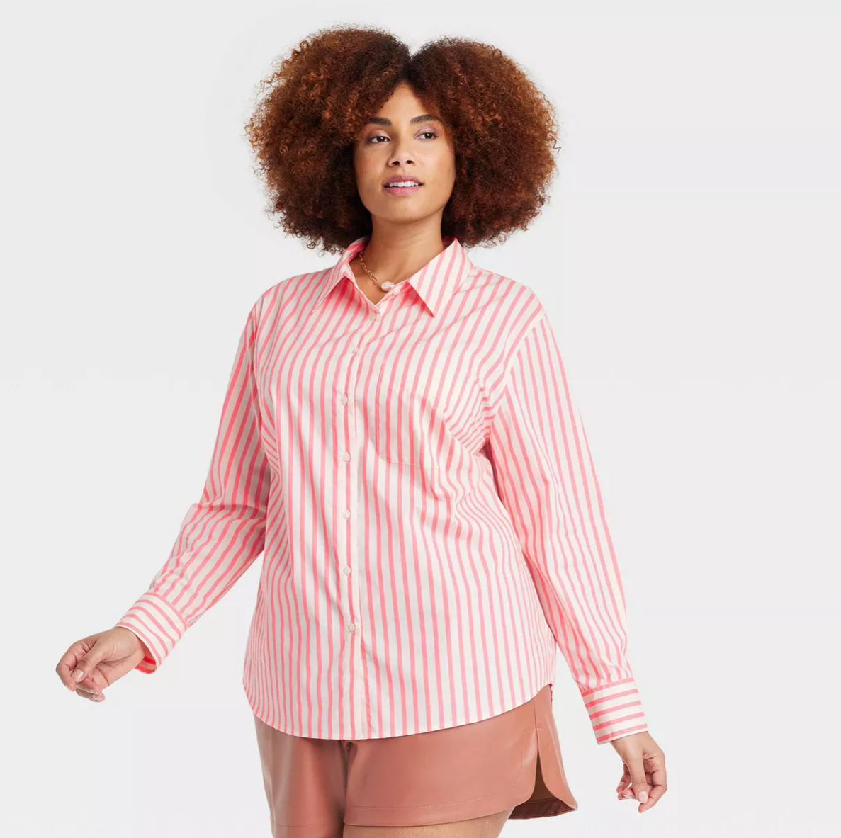 A person with curly hair is wearing a long-sleeve, striped button-down shirt and shorts