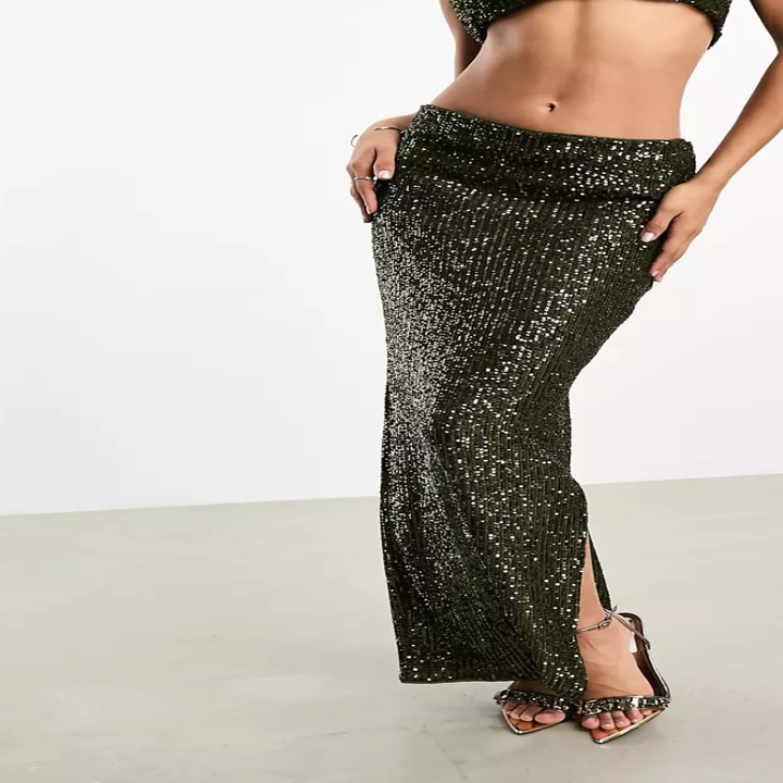 A person modeling a sparkly, form-fitting, two-piece outfit with a high-waisted, long skirt and strappy high heels