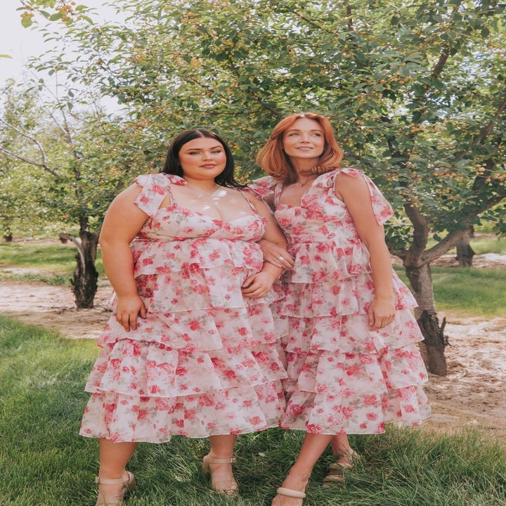 Two women stand outdoors in floral tiered dresses, showcasing fashionable summer attire