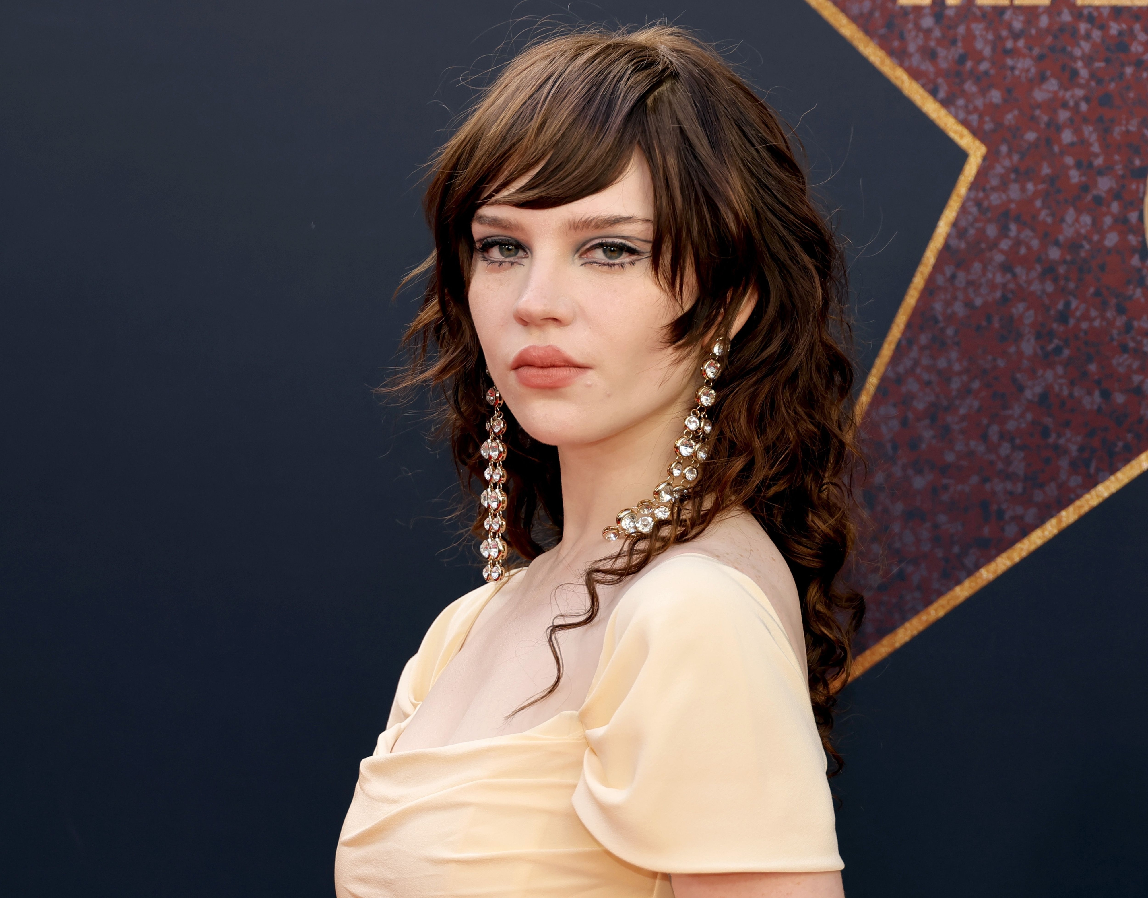 Sophie Thatcher wearing a yellow outfit and long earrings at the premiere of "MaXXXine"