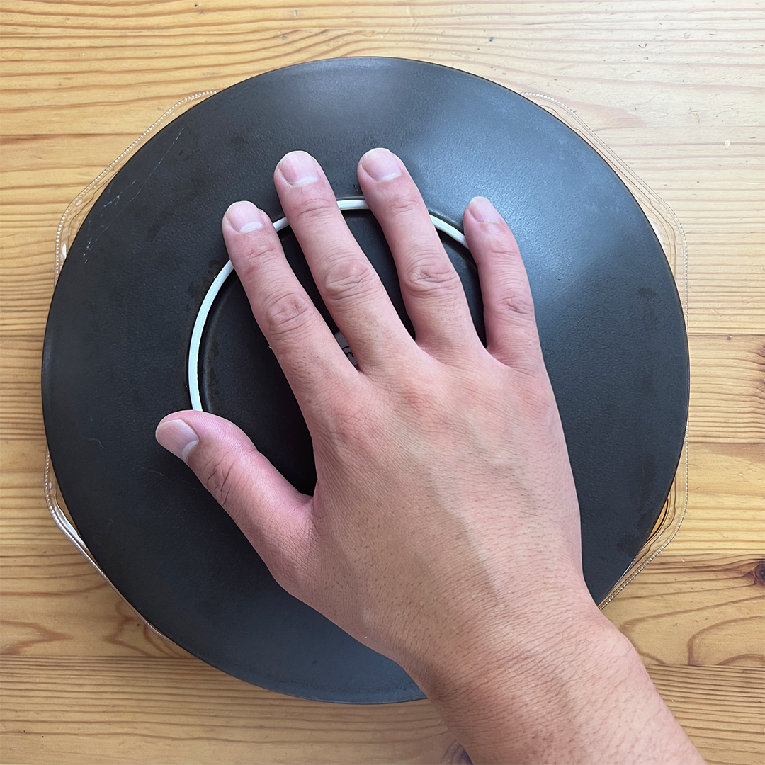 手が黒い皿の上に置かれている画像。テーブルが背景にある。