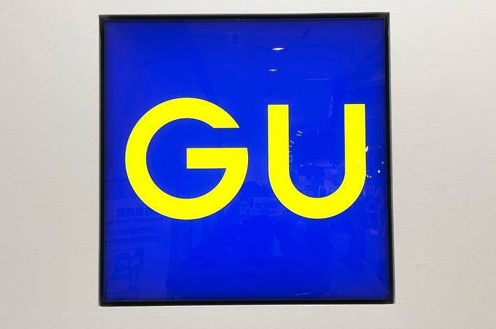 Blue square with the yellow letters “GU” in the center, displayed on a white wall