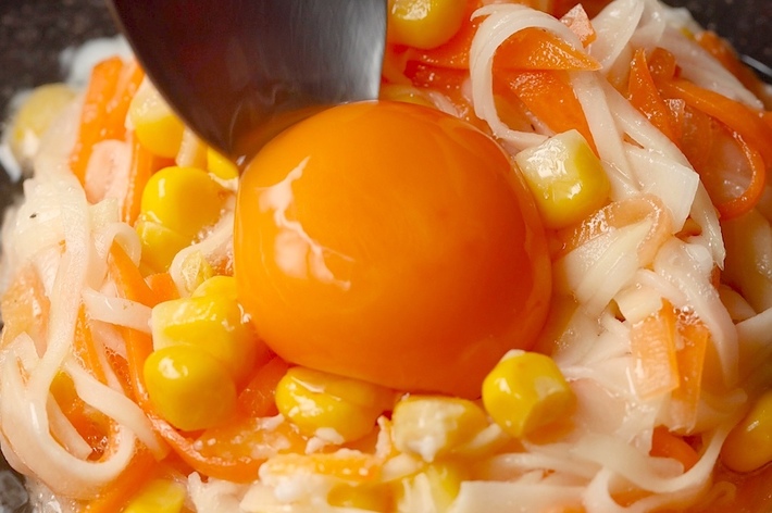 スプーンで盛り付けられたラーメンサラダに生卵の黄身がのせられています。