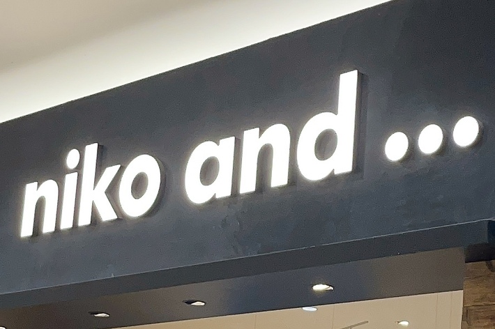 The image shows the storefront of &ldquo;niko and&hellip;&rdquo; a retail store selling clothes, accessories, and home goods. The store has a wooden facade with various items displayed