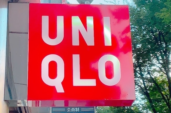 Uniqlo store sign hanging outside a building with trees visible in the background