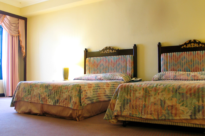 ホテルの客室にある2つのシングルベッド。ベッドは豪華なヘッドボードとカラフルな掛け布団で飾られています。