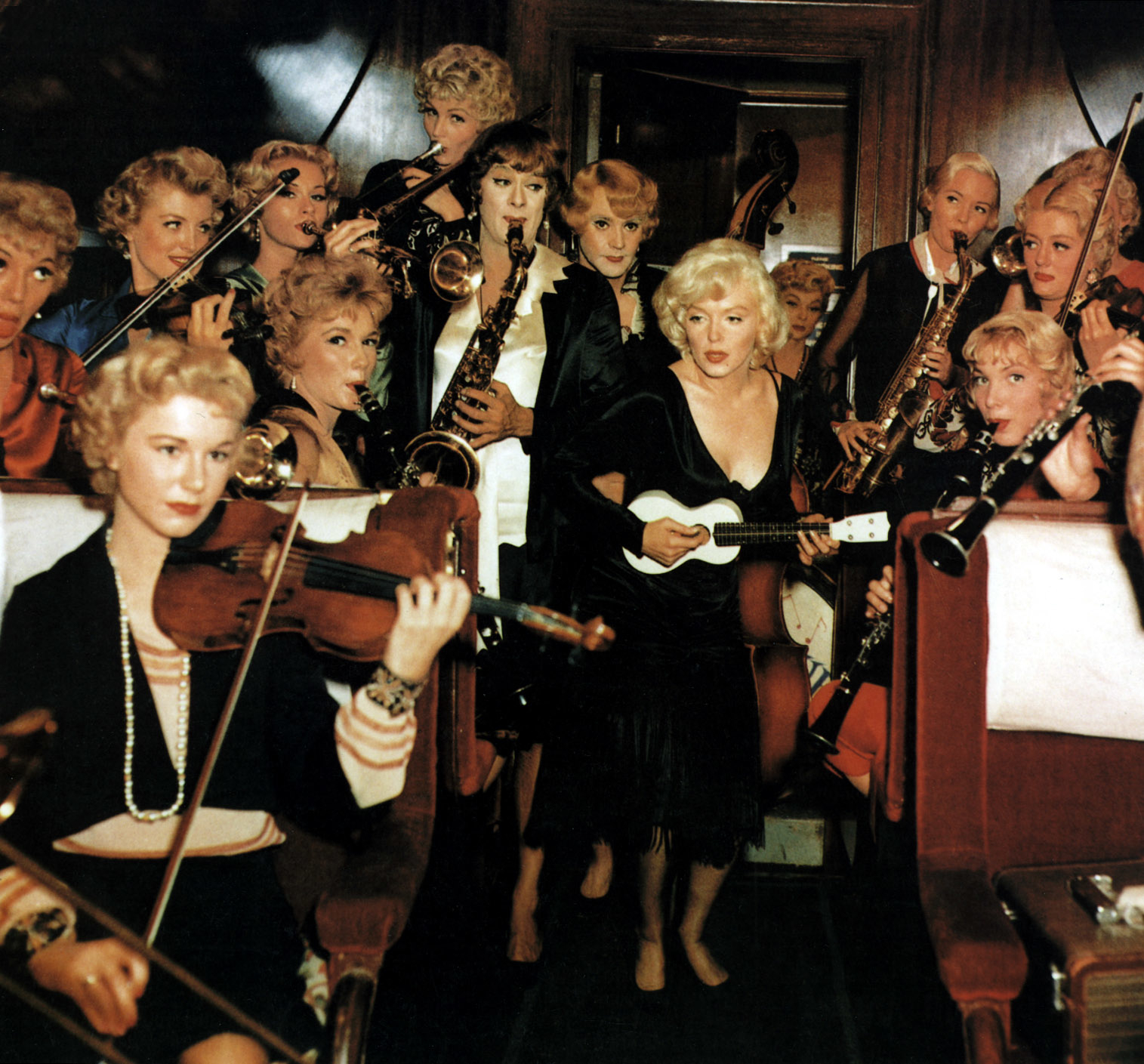 Marilyn Monroe playing a ukulele surrounded by a group of women musicians playing various instruments in the movie "Some Like It Hot."