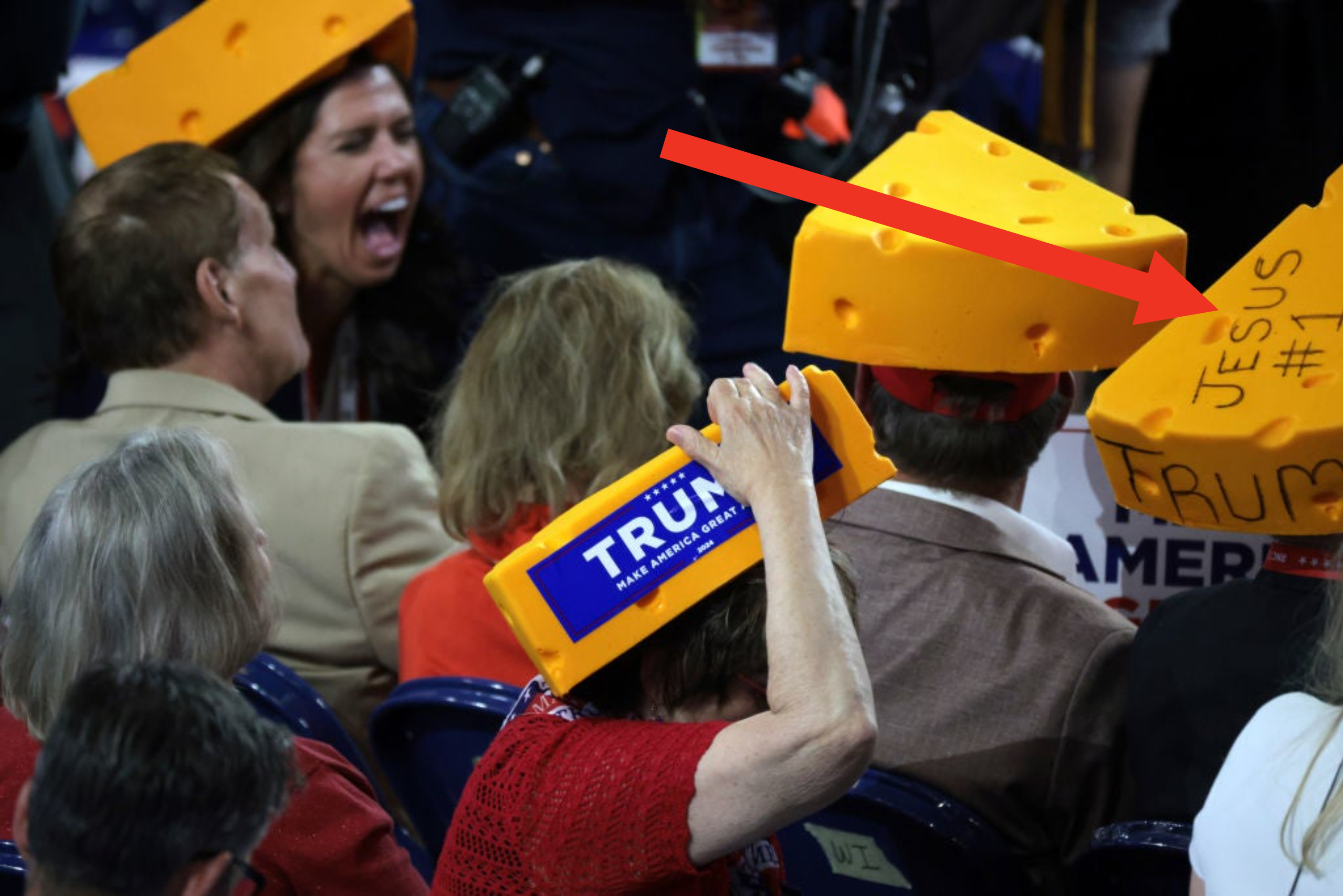 People wear cheese-shaped hats, some with &quot;Trump&quot; stickers, at a political rally. A woman yells in the background