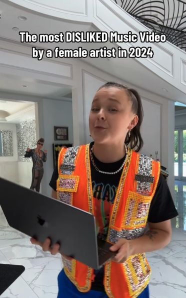 JoJo Siwa in embellished vest holds laptop indoors; text reads: &quot;The most DISLIKED Music Video by a female artist in 2024.&quot;