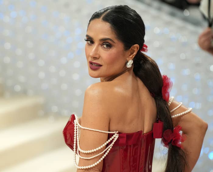 Salma Hayek on the red carpet, wearing an off-shoulder corset-style dress adorned with pearls and floral accents