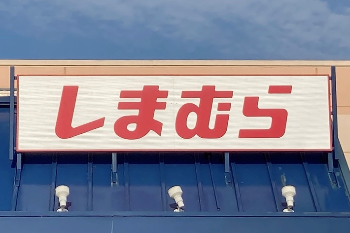 Storefront with Japanese text sign that reads &ldquo;Shimamura.&rdquo; The building&rsquo;s exterior has a blue awning and beige walls.