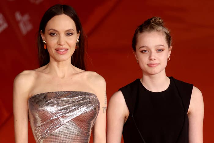 Angelina Jolie in a strapless metallic dress and Shiloh Jolie in a sleeveless dark dress on the red carpet